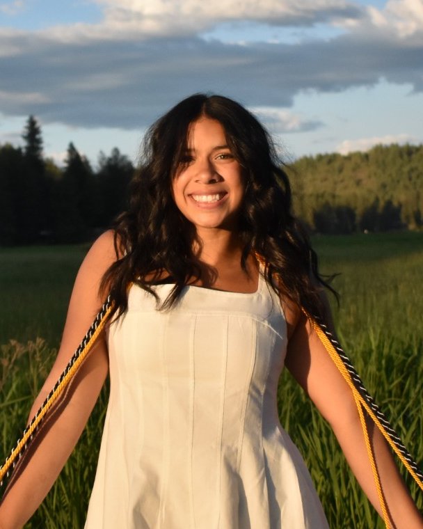 Sofia smiling in a sunny green meadow, with forest and blue sky behind her